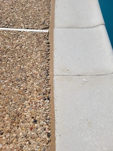 tan pool mastic with sand next to pebble deck and white stone coping